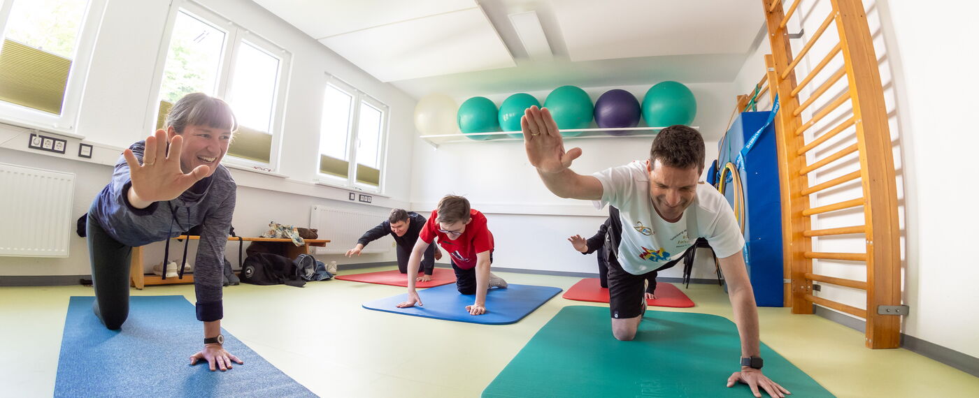 Eine Gruppe Menschen hebt im Vierfüßlerstand einen Arm und das gegenüberliegende Bein.
