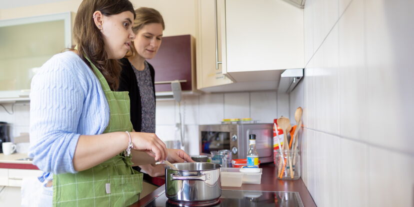 Eine Teilnehmerin und eine Lehrkraft stehen an einem Herd und kochen.