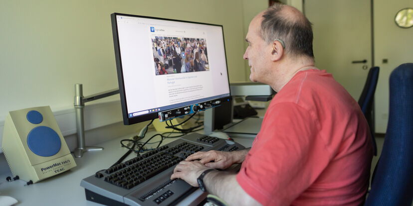 Ein Mann sitzt vor einem Computer und bedient eine Punktschrift-Tastatur.