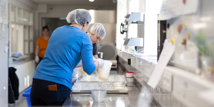 Zwei Mitarbeiterinnen verteilen in der Küche Dessert in Glasschüsseln.
