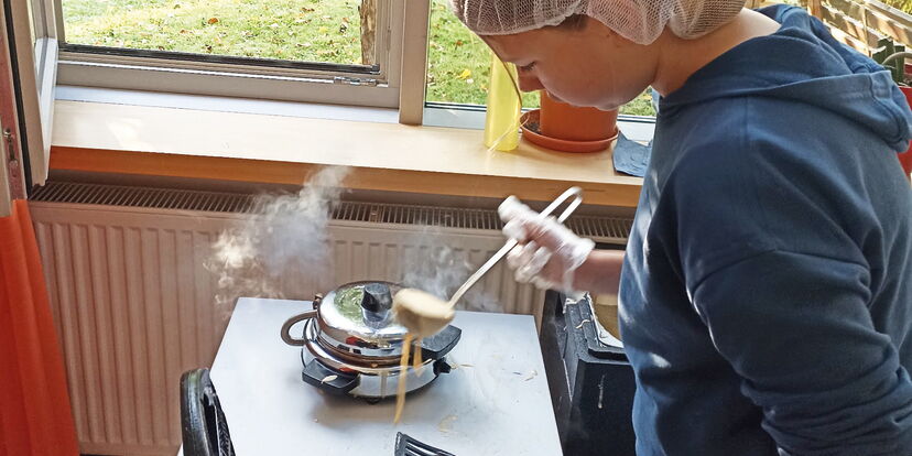 Eine Schülerin füllt Teig mit einer Schöpfkelle in ein Waffeleisen.