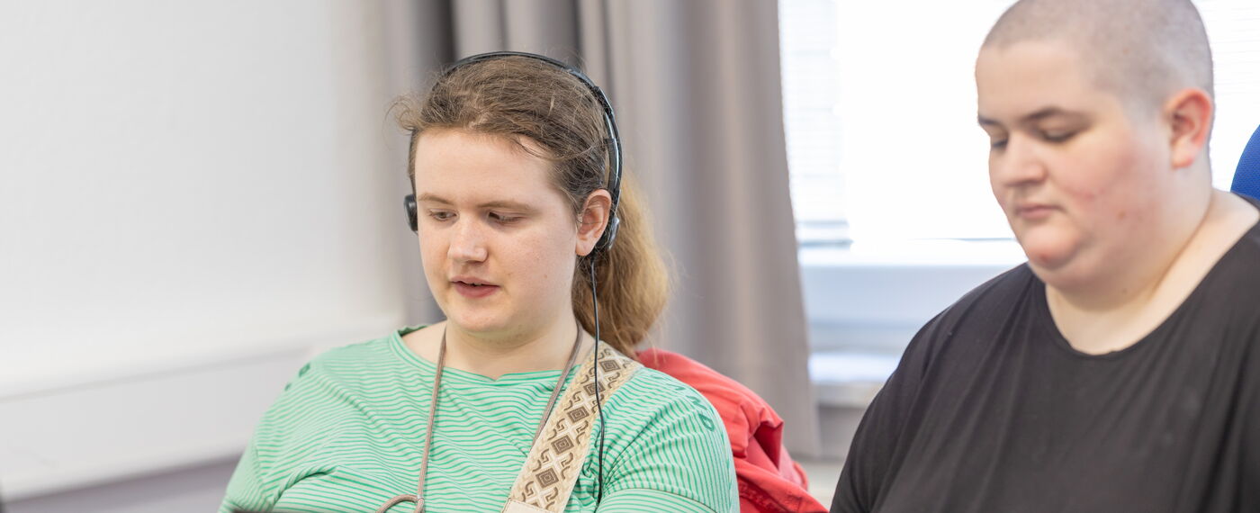 Zwei Azubis sitzen vor Laptops, eine der beiden trägt Kopfhörer