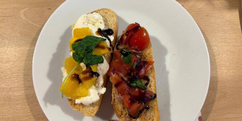 Auf einem Teller liegen zwei Brote: eine Mango-Mozzarella-Bruschetta und eine mit Tomaten.