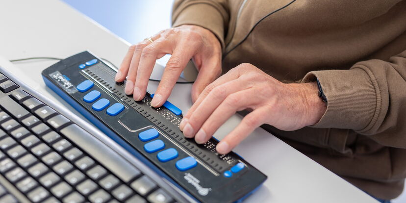 Zwei Hände lesen Punktschrft auf einer Braillezeile.