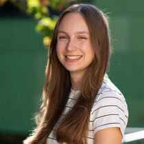 Portraitfoto Marie Mattheis - Sie trägt langes, glattes dunkelblondes Haar und ein weißes T-Shirt mit schwarzen Streifen.