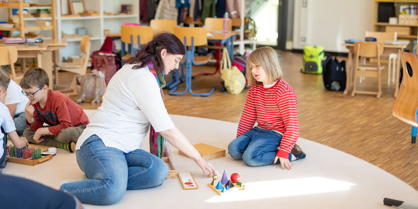 Eine Lernbegleitung sitzt mit Kindern auf dem Boden und demonstriert Material.