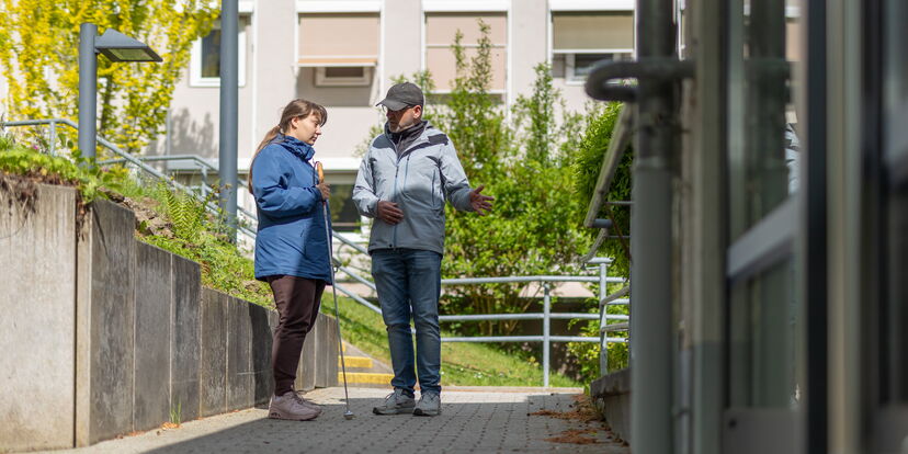 Auf dem blistaCampus: Ein O&M Lehrer erläutert einer Frau mit Langstock etwas.