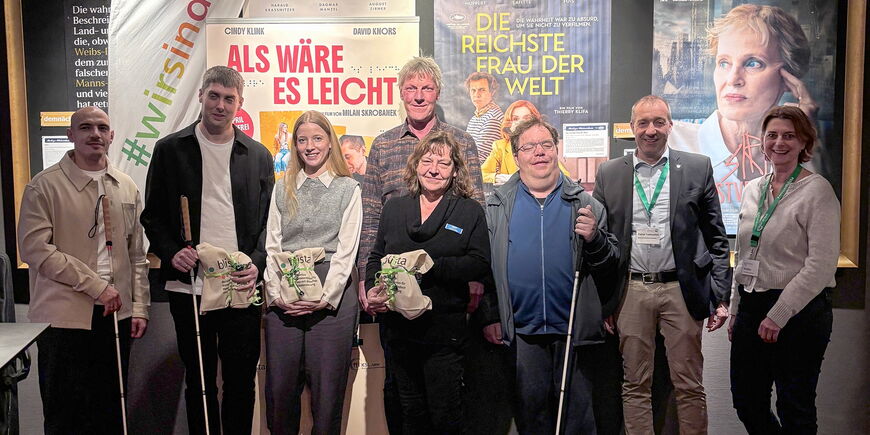 Vor einer blista-Beachflag und Filmplakaten stehen acht Personen, teil mit Langstöcken und Geschenken.