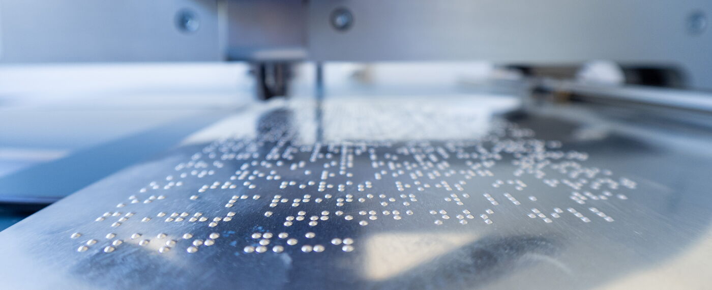 Nahaufnahme: Auf eine Matrize aus Blech ist Punkschrift geprägt.