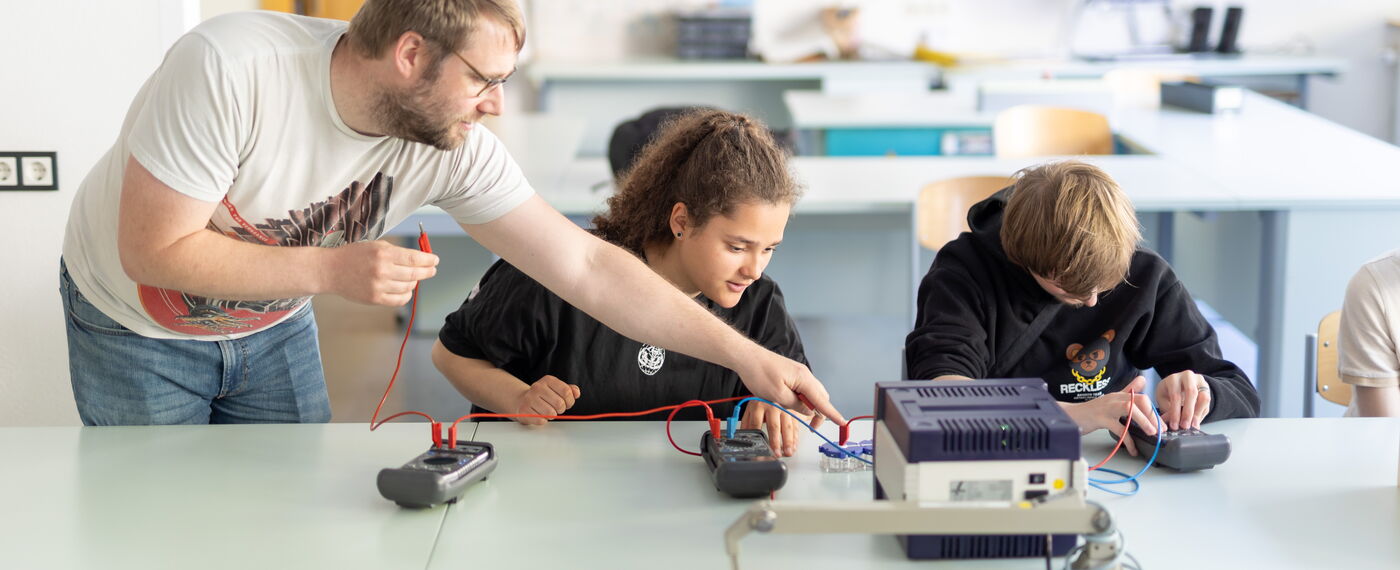 Zwei Schül*innen und ein Lehrer im Physikunterricht