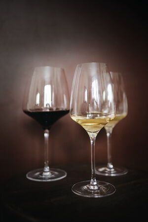 Drei Weingläser mit Rot-und Weißwein vor einem dunklen Hintergrund.