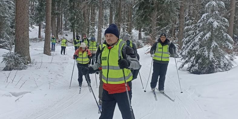 Ausgerüstet mit Langlaufskiern und den gelben Warnwesten fährt die Gruppe aus einem Waldstück heraus.