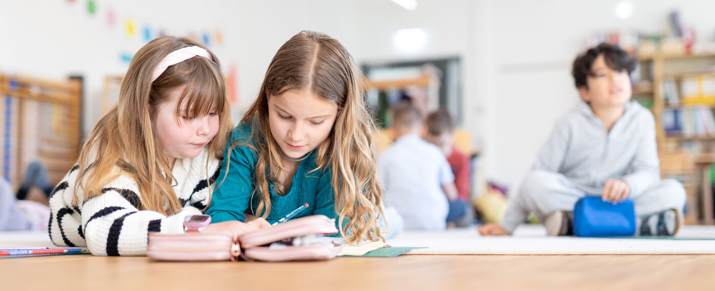 Zwei Schülerinnen arbeiten gemeinsam auf dem Boden liegend.