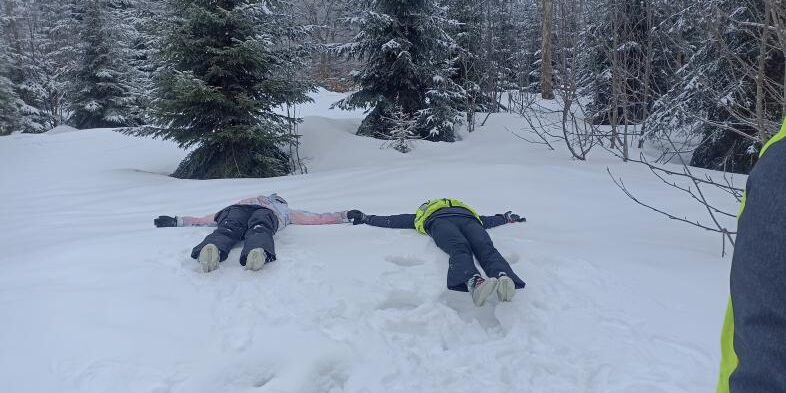 Zwei Menschen liegen im Schnee und scheinen Schneeengel zu machen.