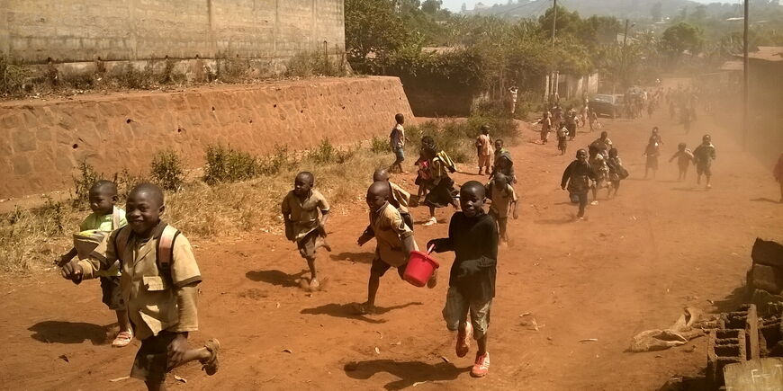 Auf einer lehmigen und staubigen Straße laufen Kinder. mache halten Eimer und andere Gegenstände in der Hand.