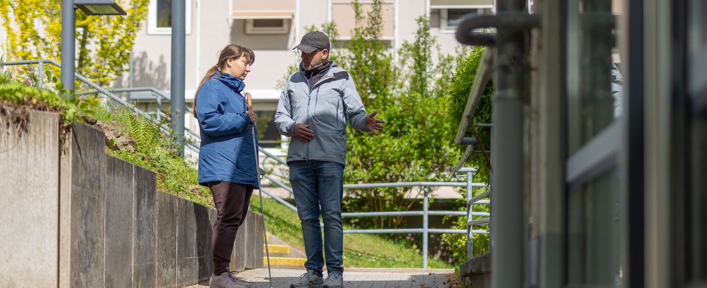 Auf dem blistaCampus: Ein O&M Lehrer erläutert einer Frau mit Langstock etwas.