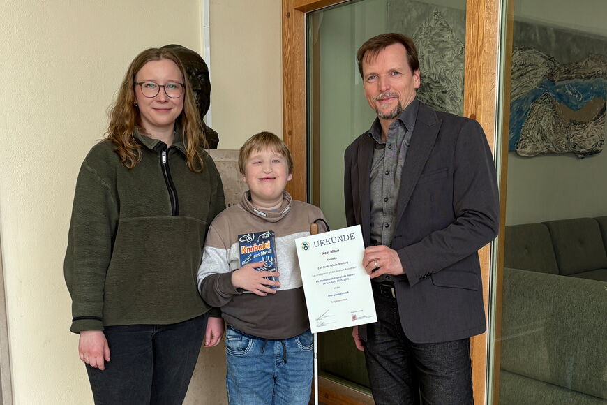 Im Foyer der CSS überreicht Schulleiter Peter Audretsch Noel eine Urkunde gemeinsam mit Debora Debes.