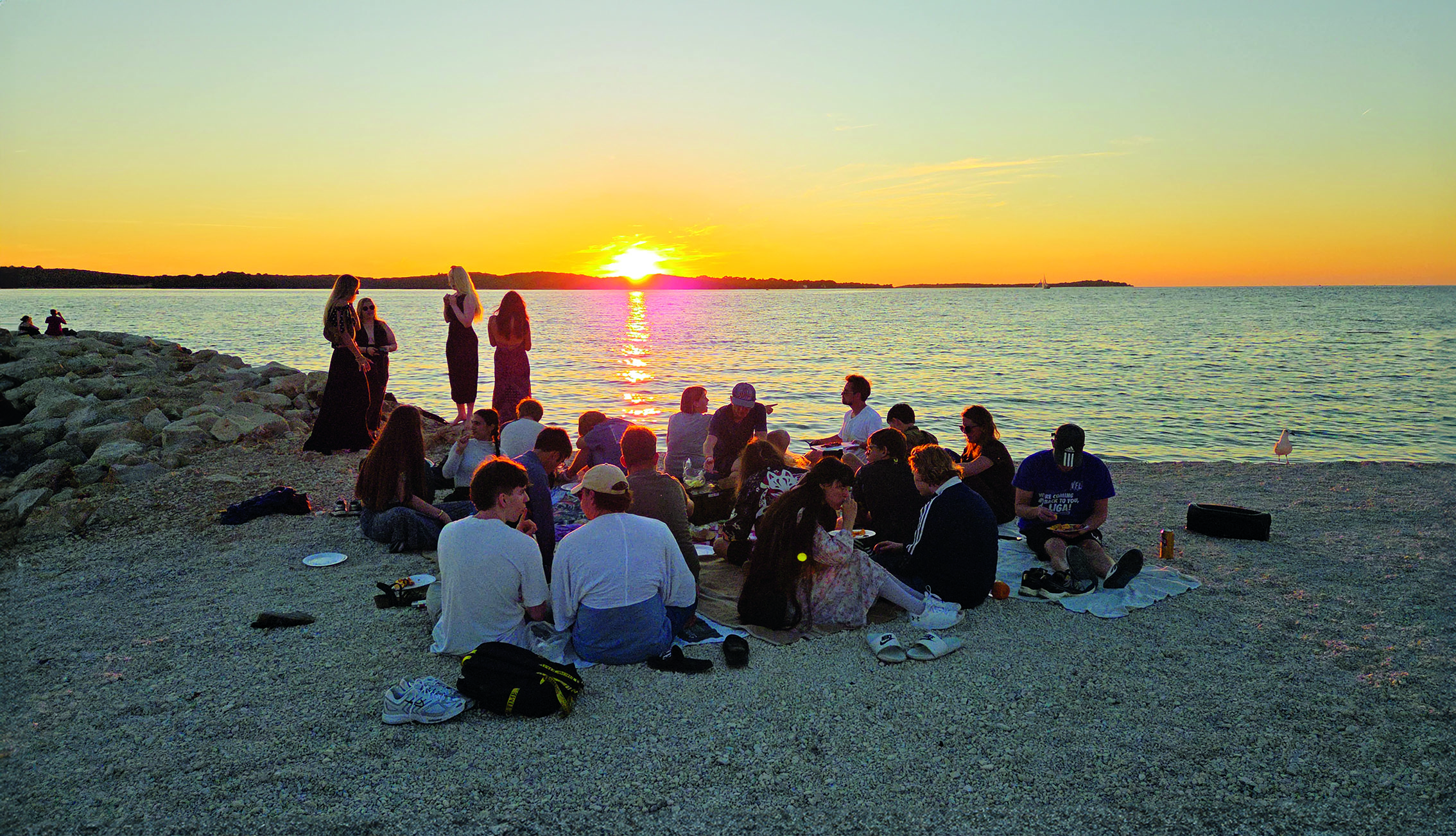 Traumhafte Aussicht am Abend, die Gruppe trifft sich zu einem Picknick am Strand, während die Sonne über der Adria untergeht.