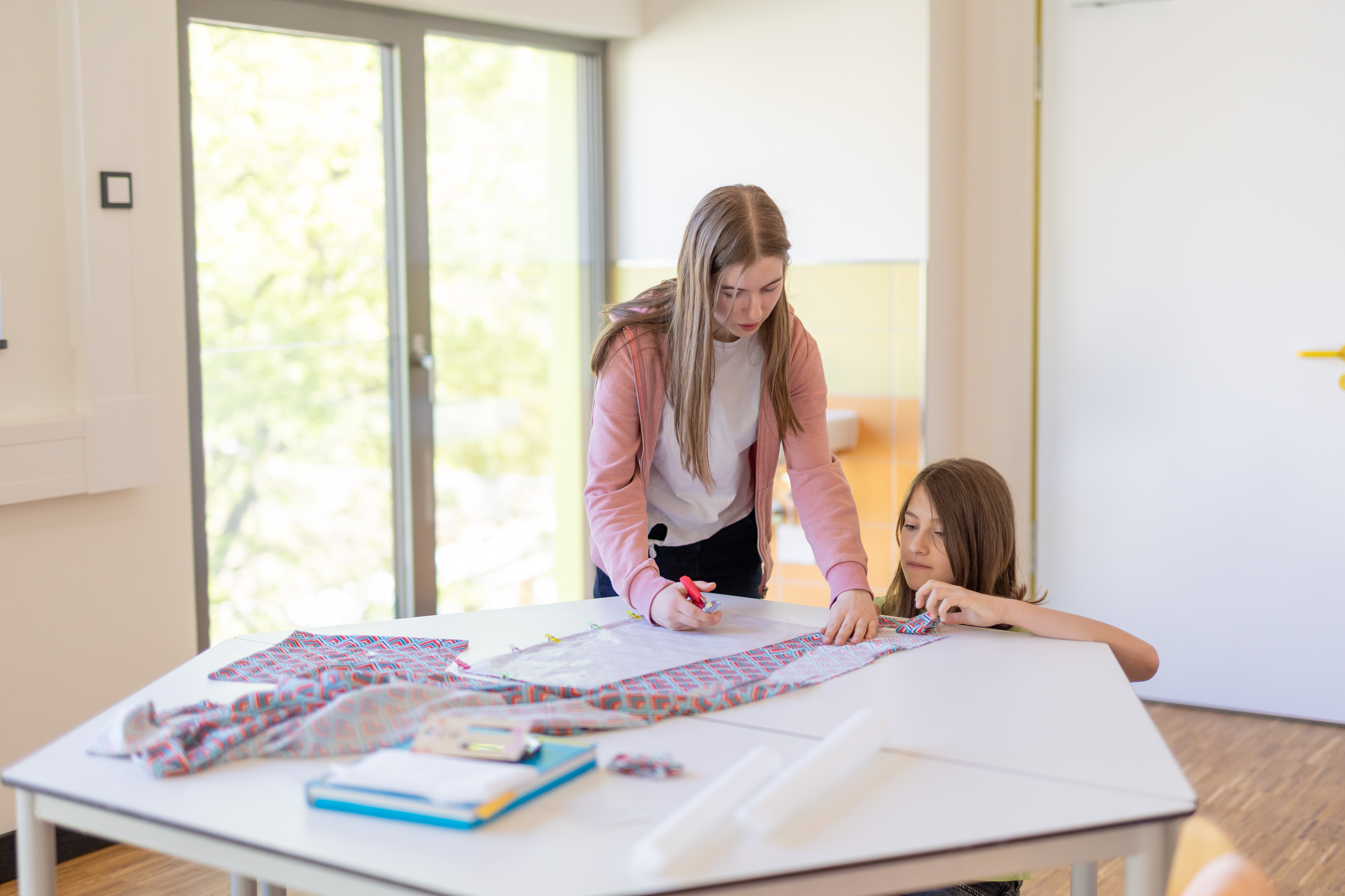 Zwei Schülerinnen schneiden eine Stoffbahn.