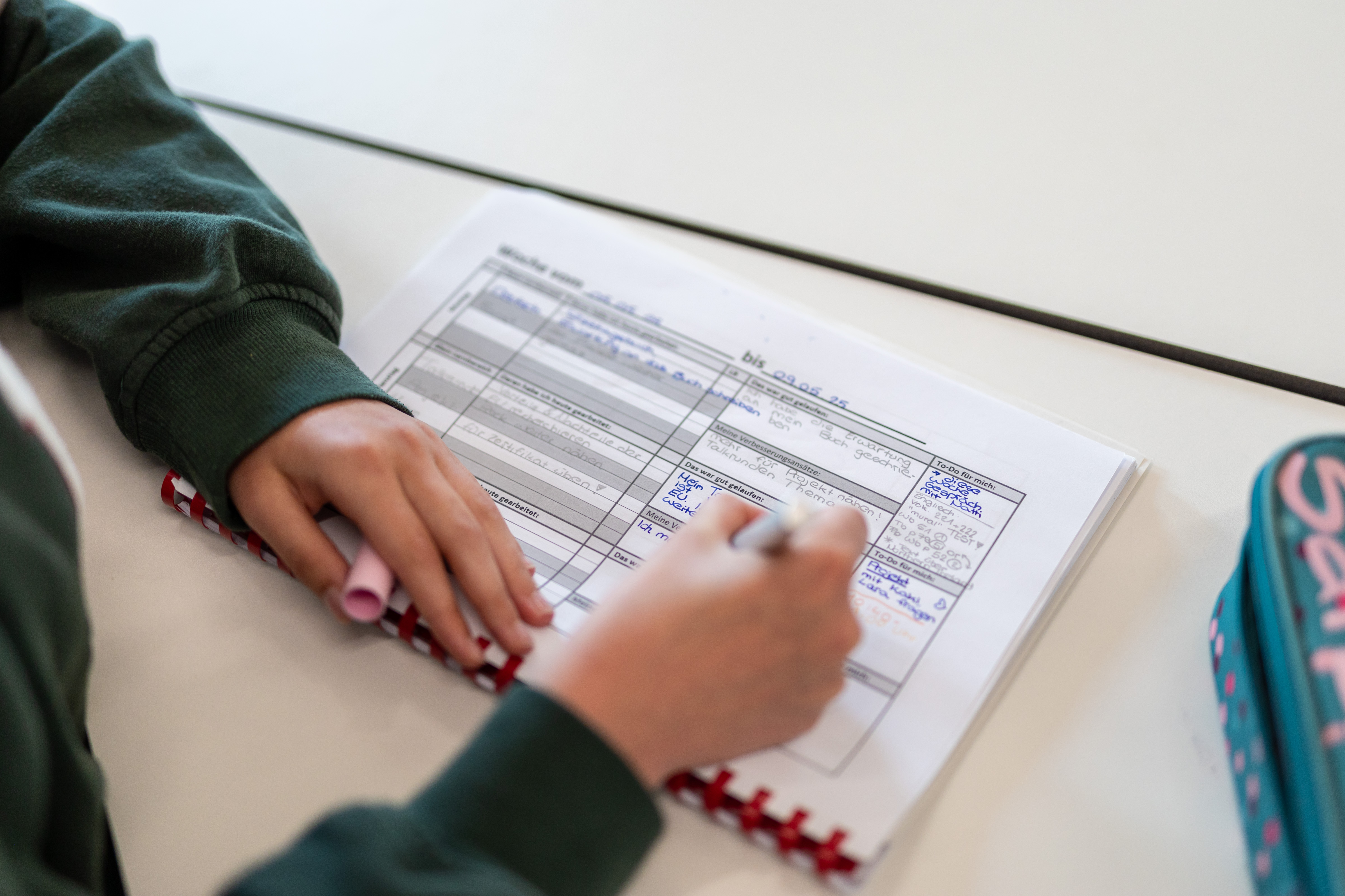Eine Hand füllt einen Wochenplan-Zettel aus.